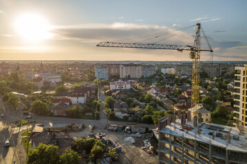 Apartment or office tall building under construction. Brick walls, glass windows, scaffolding and concrete support pillars. Tower crane on bright blue sky copy space background.