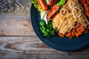 Fish dish - fried fish fillet on vegetable sauce on wooden table

