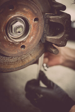 Mechanic working at a car worn and rusty brake disk and caliper