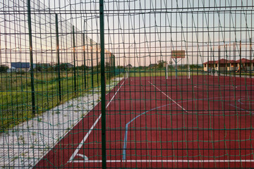 Outdoors mini football and basketball court with ball gate and basket surrounded with high protective fence.