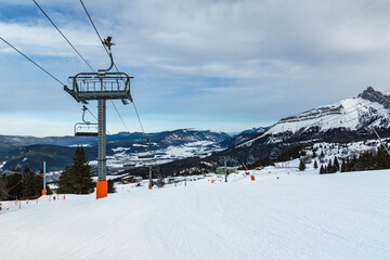 Fototapeta na wymiar Empty chair lift at french Villard de Lans ski resort surrounded by snowy Vercors mountains.