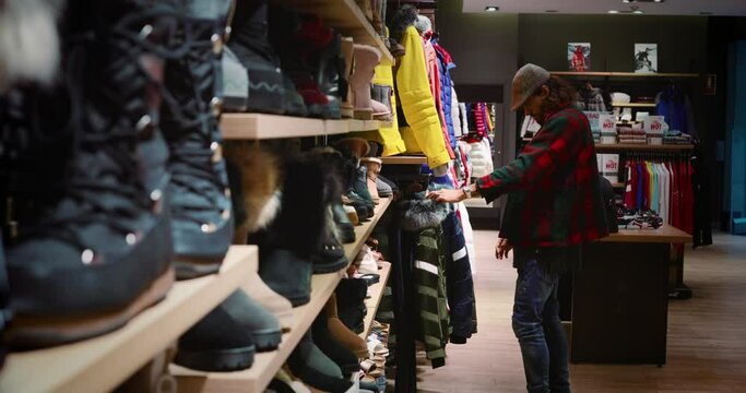 Man goes shopping and looks at clothes during winter vacation. We can see winter clothes, perfect to go skiing in the mountains 4K