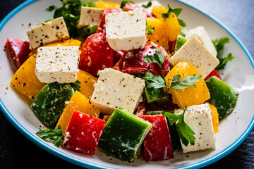 Fresh Greek salad - feta cheese, tomatoes, cucumber, three color pepper, black olives and onion on black stone board
