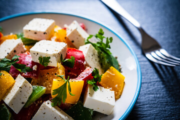 Fresh Greek salad - feta cheese, tomatoes, cucumber, three color pepper, black olives and onion on black stone board
