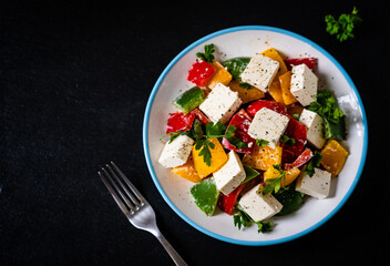 Fresh Greek salad - feta cheese, tomatoes, cucumber, three color pepper, black olives and onion on black stone board

