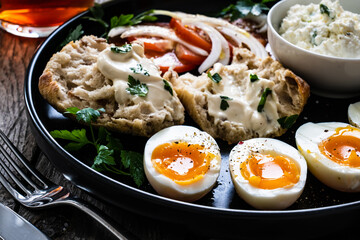 Delicious breakfast - soft boiled eggs with  cottage cheese and vegetables served on black plate on wooden table
