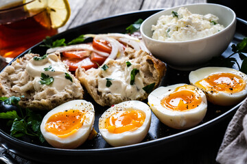 Delicious breakfast - soft boiled eggs with  cottage cheese and vegetables served on black plate on wooden table
