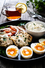 Delicious breakfast - soft boiled eggs with  cottage cheese and vegetables served on black plate on wooden table
