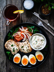 Delicious breakfast - soft boiled eggs with  cottage cheese and vegetables served on black plate on wooden table
