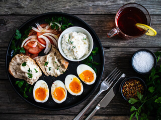 Delicious breakfast - soft boiled eggs with  cottage cheese and vegetables served on black plate on wooden table
