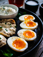 Delicious breakfast - soft boiled eggs with  cottage cheese and vegetables served on black plate on wooden table
