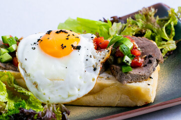 Italian bruschetta with egg and meat on a ceramic blue tray.