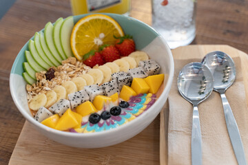 Healthy smoothie bowl breakfast with granola, cut banana, sliced apples, strawberries, and various types of nuts