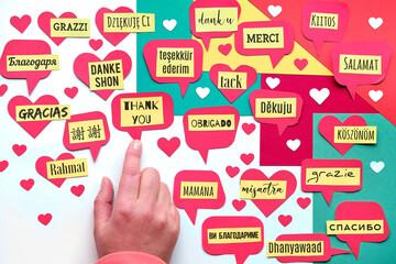 Thank You in many languages. Paper art, creative flat lay, top view on paper tags. International Thank you day. Creative background on colored paper. Hand point at Thank You text tag in English.