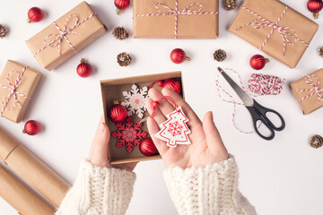 Pov top above close up overhead view photo of female hands holding showing box with christmas decor demonstrating hanging tree snowflakes over white working place