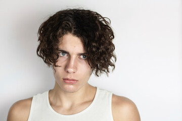 Natural portrait of a teenage boy with long curly hair on a light background. The boy had a difficult childhood and when he remembers it he is always sad as now