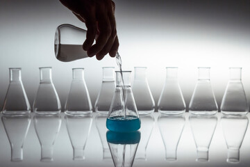 Hand pouring white in to blue liquid in scientific laboratory glass erlenmeyer flask with glassware...
