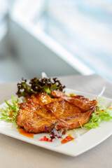 main course of Pan-fried Pork Chop with Soy Sauce served on lettuce on a white plate