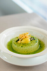 main course of Simmered Winter Melon in Spinach Sauce topped with a gingko nut served in a white bowl