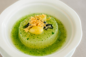 main course of Simmered Winter Melon in Spinach Sauce topped with a gingko nut served in a white bowl