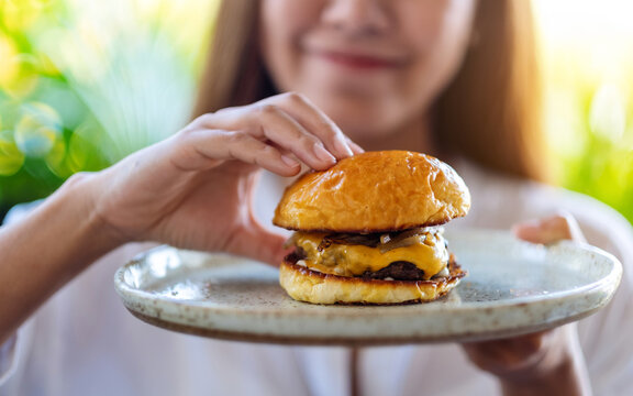 Closeup image of a beautiful woman grabbing and eating beef hamburger in a plate