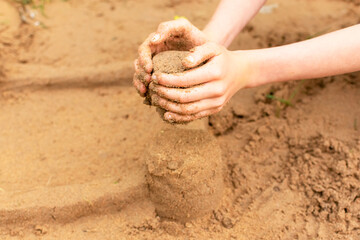 A child builds sand castles on the beach in the summer. Sea tour. Child's hands in the sand. Entertainment in the fresh air..