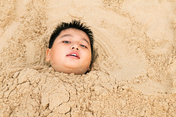 Young boy buried in sand on the beach