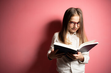 A little girl with European appearance, long hair and glasses is reading a book