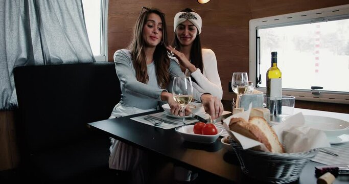 Twins women eat a lunch in winter holidays, with cheese, meat and french white wine. The women serve and drinks white wine. Perfect meal in a mountain restaurant 4K