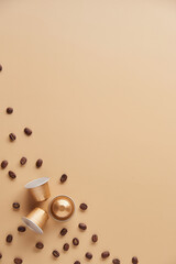 Caffeine, hot drinks and objects concept - close up of golden capsules or pods for coffee mashine with some roasted grains on beige background. Top view with space for text. Flat lay..