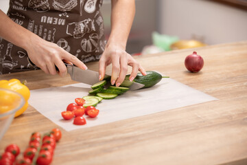 Woman's hands cutting cucumber, behind fresh vegetables.
