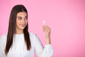 Satisfied  woman touches menstrual cup with pleasure, stands with flexible menstrual cup to insert in vagina during periods, protects from blood leakage, isolated on pink background