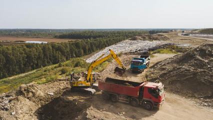 Obraz premium Excavation pit. Digger and trucks on dirt road. Top drone view. Heap of sand and stones.