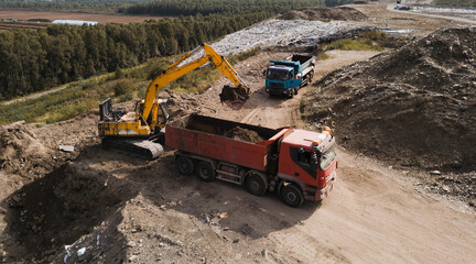 Excavation pit. Digger and trucks on dirt road. Top drone view. Heap of sand and stones.