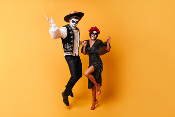 Obraz premium Portrait in full growth of dancing funny men and his sweet lady. Girl with crown of roses and painted face is enjoying Halloween with her boyfriend