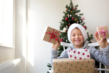 Obraz na płótnie Canvas Happy boy in santa clause hat with Christmas gifts