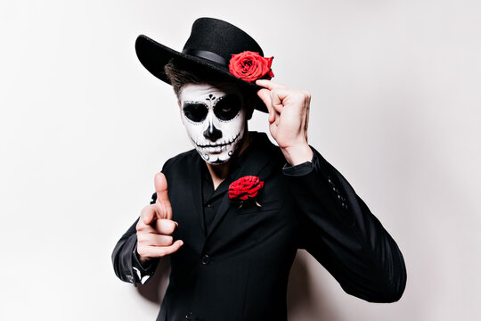 Mexican man in black outfit is posing, imagining himself mafia. Close-up shot of extraordinary guy with skull mask