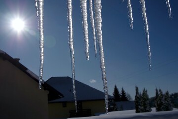 A icicles lit by the sun's rays hangs from the roof on a sunny winter day