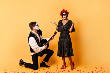 guy in classic trousers sings serinade with guitar to his surprised girlfriend. Full-length shot of...