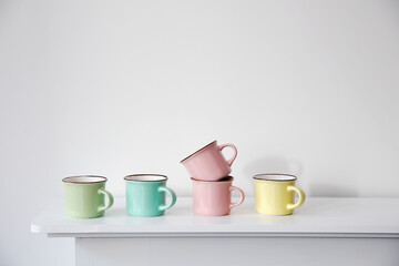 FIVE small multicolored pastel coffee cups on a white console against a wall background