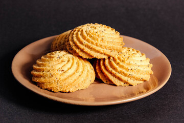 Fresh shortbread cookies with poppy seeds on a saucer on a black background.