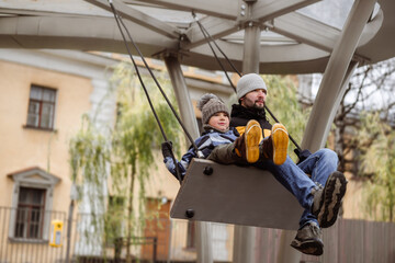 father with cute 6 year old son swinging on large bench swings. brothers with dad walking on playground