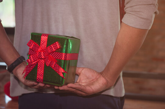 Man standing and holding valentine's gift box behind his back for surprise his lovely girlfriend..Close up of man standing and holding gift box behind his back. Making surprise concept