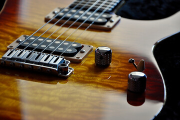 Selective focus on the tone knob and pickups located on the top of a quilted maple on mahogany, cherry burst electric guitar.