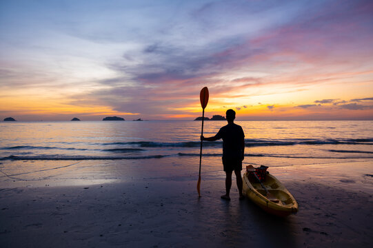 A man is looking at the sea while sunset with holding paddle and stay near Kayak.