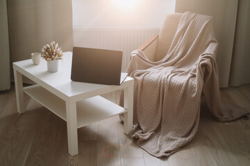 Cozy living room interior of freelancer, comfortable domestic workplace. Laptop and cozy chair with plaid. Remote work at home 