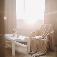 Cozy interior with coffee table, armchair and plaid near window. Sunny living room. Scandinavian interior. Slow living concept