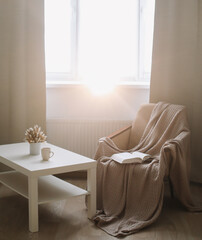 Cozy interior with coffee table, armchair and plaid near window. Sunny living room. Scandinavian interior. Slow living concept