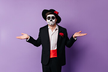 Guy with mask of skull spreads his hands, not being able to help in any way. Portrait of man in disbelief posing on isolated background