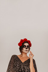 Mexican girl with roses in wavy hair mysteriously looks into camera in white room